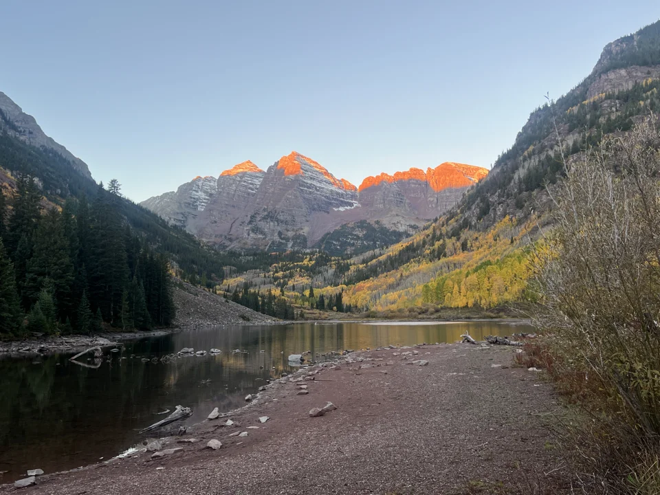 Sunrise lighting the Maroon Bells orange above Maroon Lake